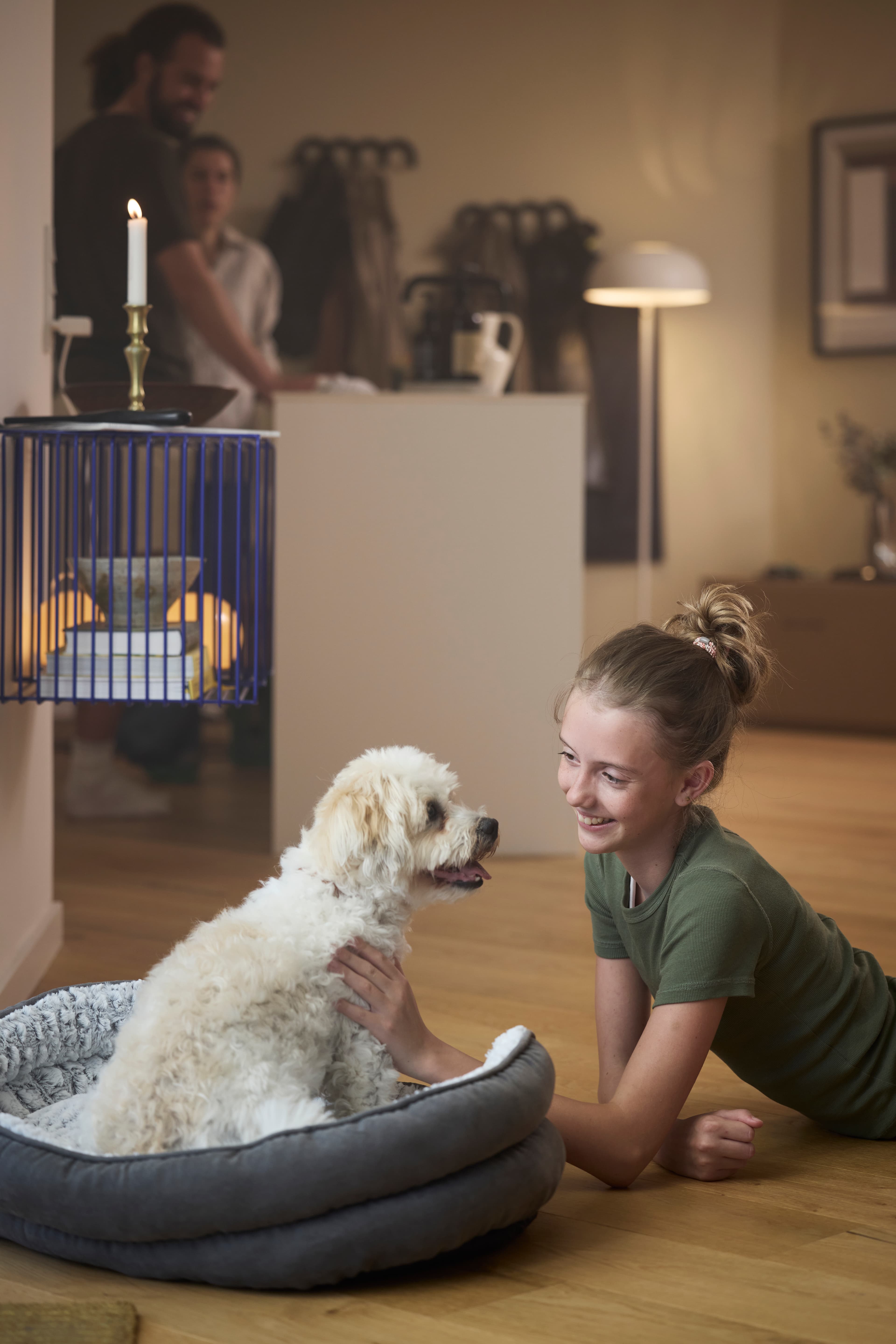 Girl lying on the floor, petting her white dog sitting in its dog bed.
