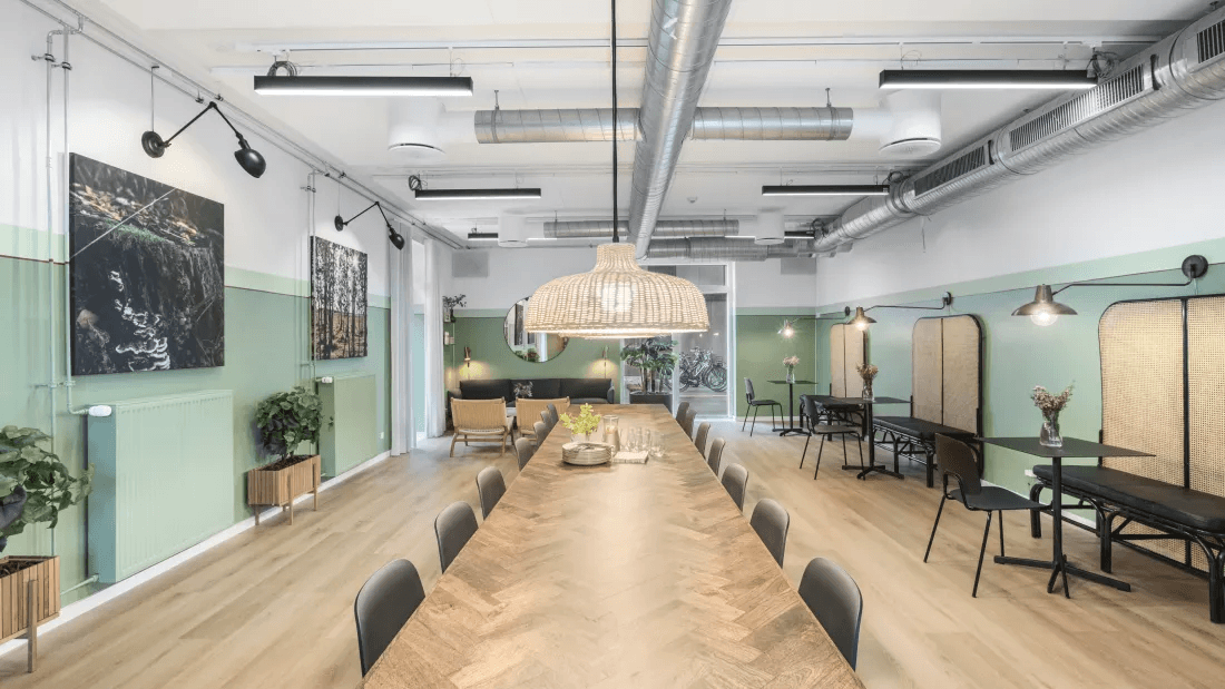 Communal room at Green Hills in Solrød with a long table, lamps and plenty of seating.