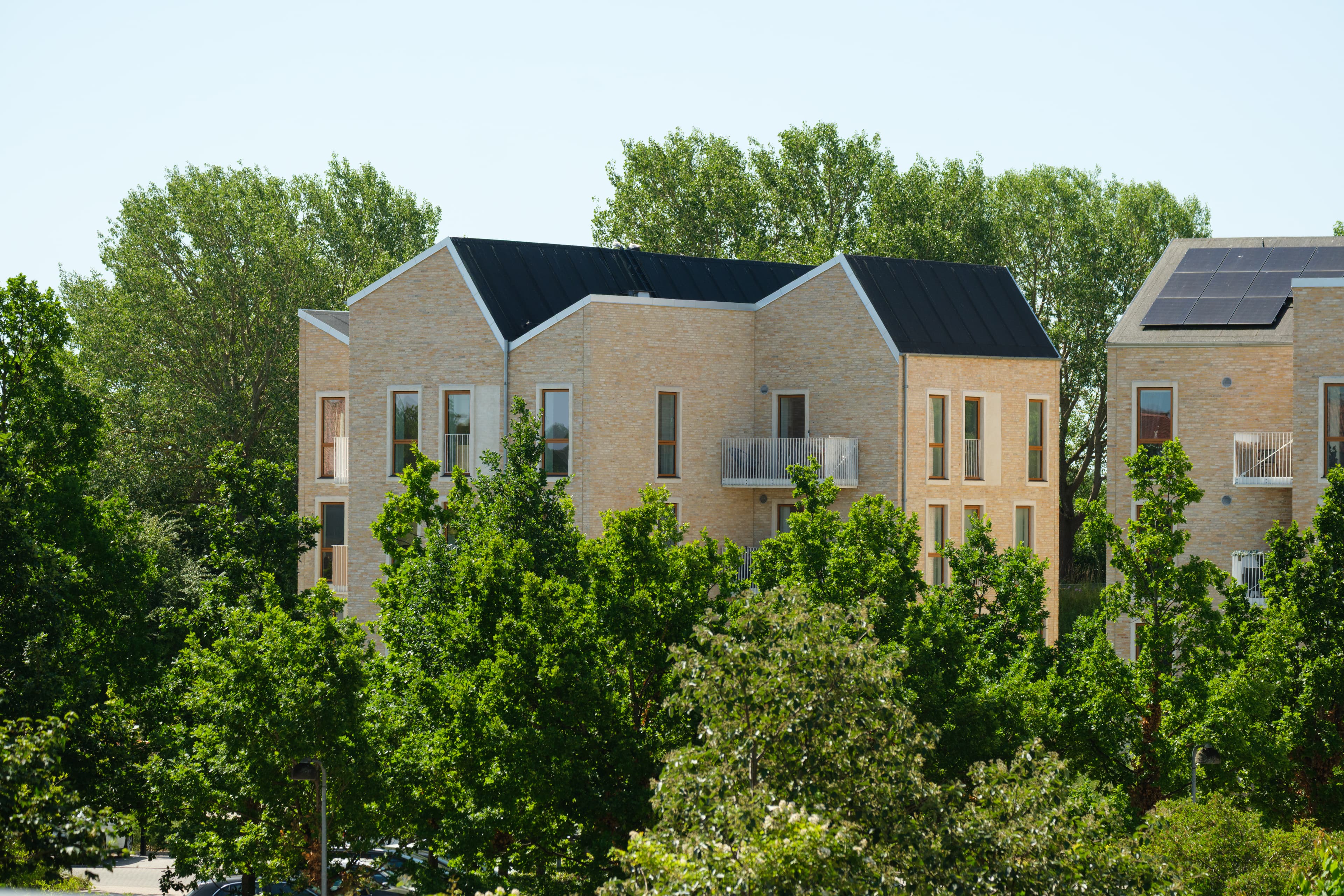 The image shows the exterior of the Strandby Høje property, featuring two buildings surrounded by landscaped green areas.