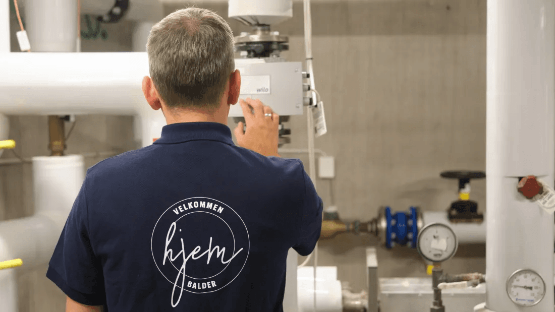 Operations technician from Balder Denmark standing by the heat pump