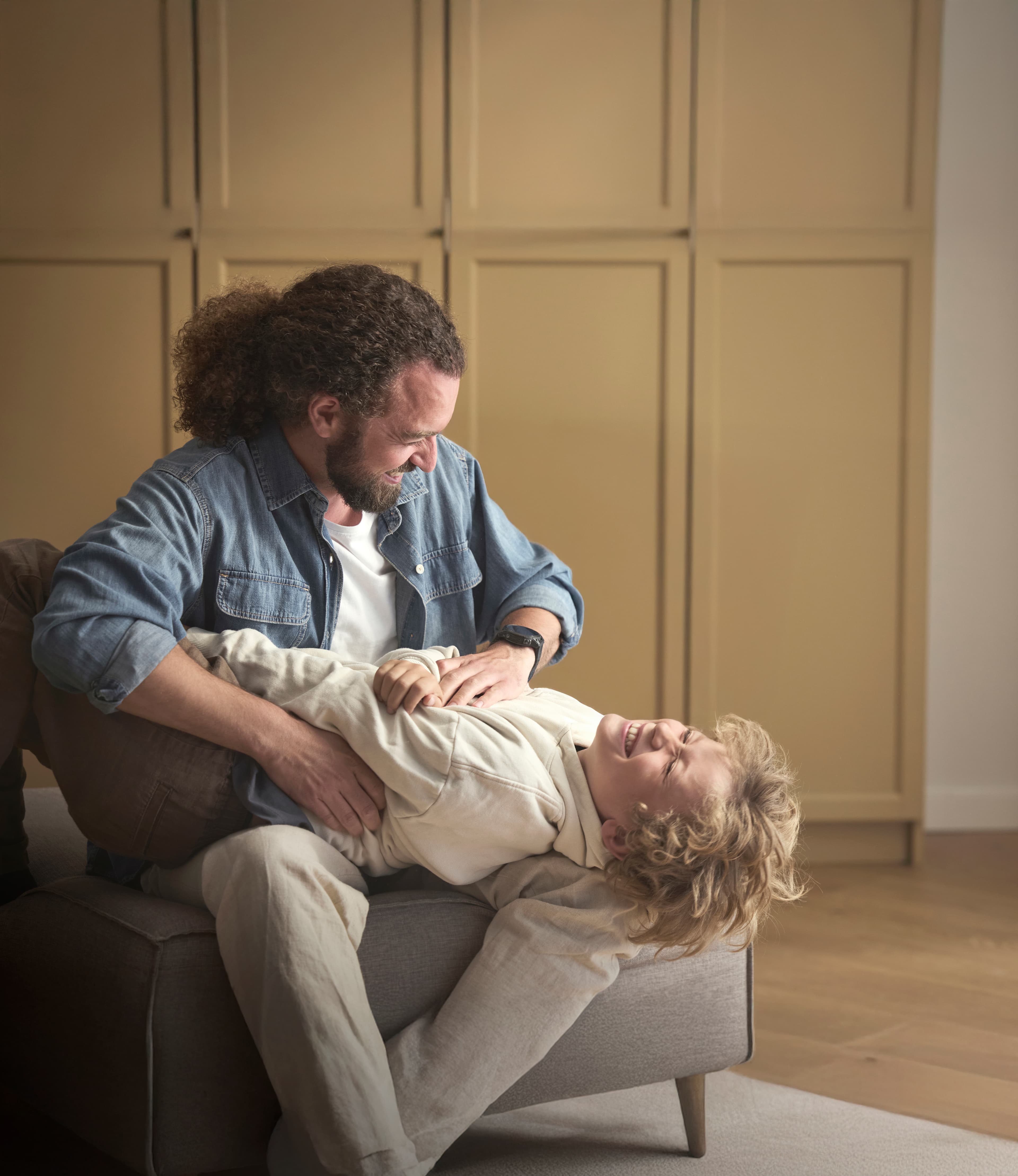 Father tickling his son on the sofa.