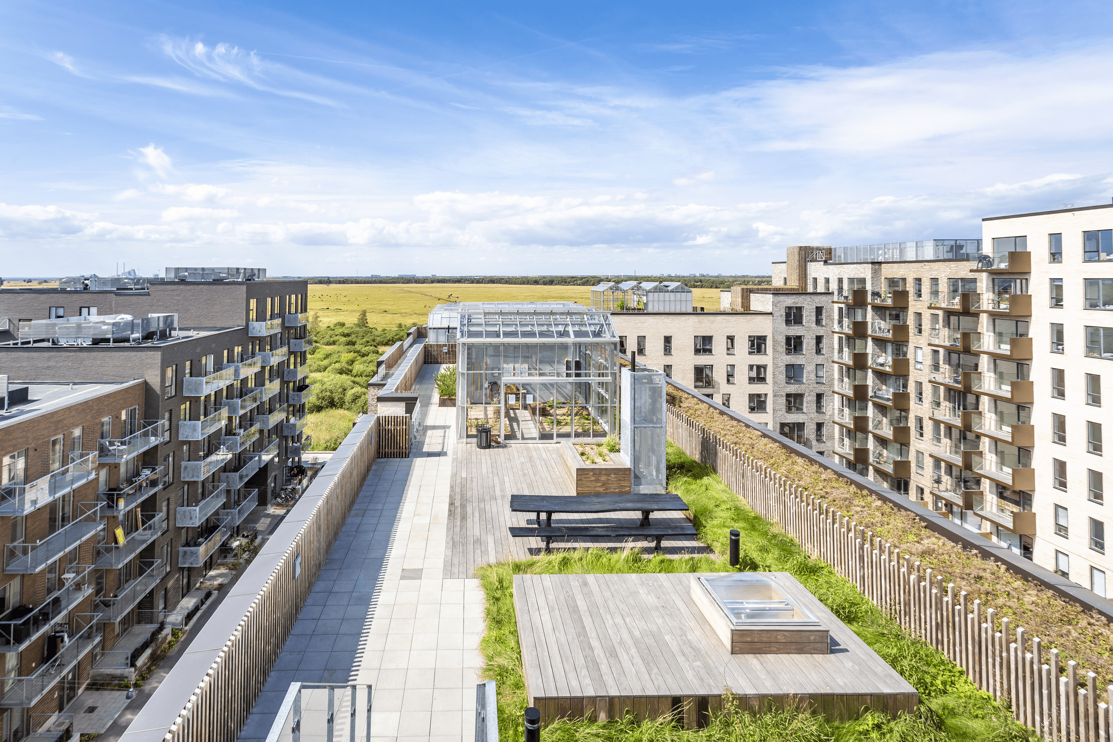 Exterior view of the rooftop terrace at Fælledkanten, featuring a greenhouse and an outdoor seating area.