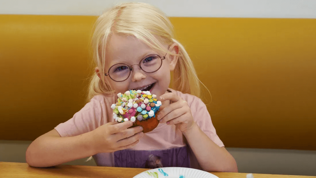 Pige med briller sidder med en cupcake og smiler